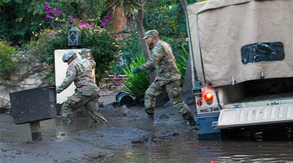 Sgts. Paiz and Espinoza of the California National Guard trudge through knee-deep mud to rescue three people and a dog trapped inside their Montecito home. Air National Guard photo by Senior Airman Crystal Housman.