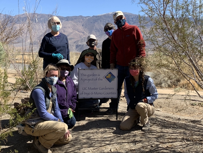 8 masked volunteers posing around a project sign