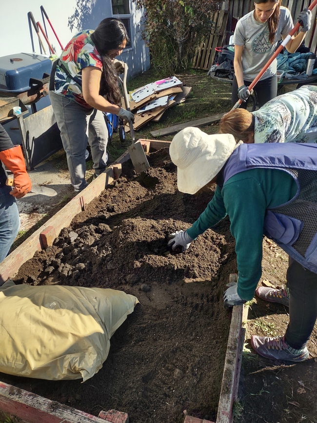 Four people add soil to a raised bed planter box.