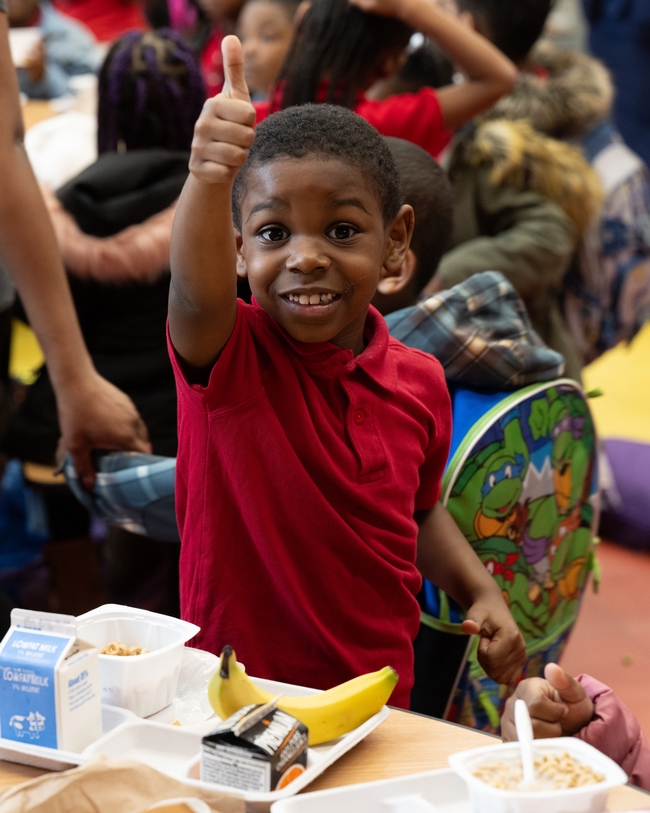 A student gives a thumbs up while eating breakfast in the school cafeteria