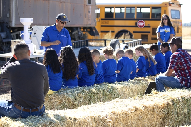 A UCCE scientist holds rice grains in his hand to show a row of schoolchildren