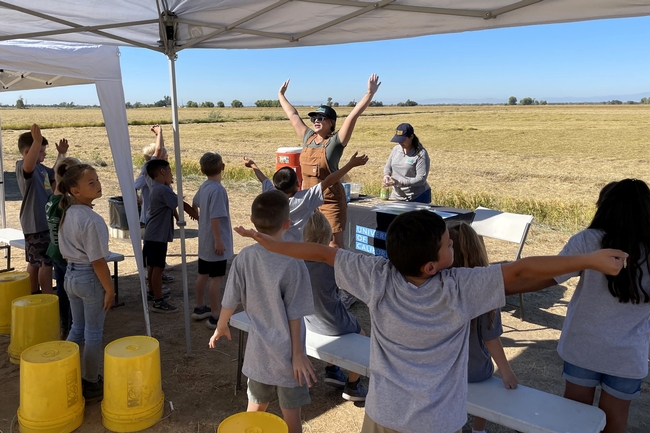 An educator leads children in a movement activity by raising her hands