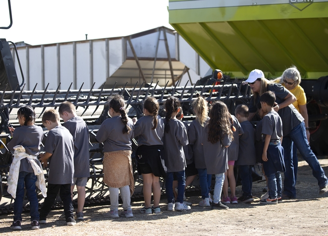 A volunteer talks with children about a header at the front of a harvester