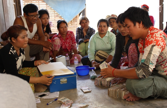 Cambodian group sits on the floor, watching as cash gets counted and recorded.