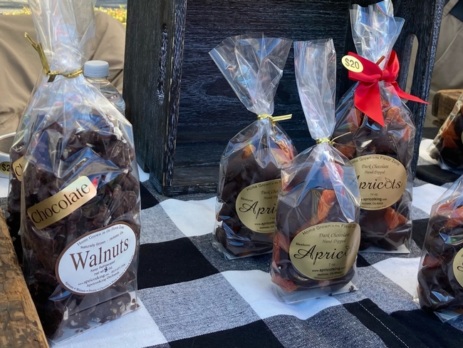 Cellophane packages of chocolate-dipped walnuts and apricots on table at farmers market.