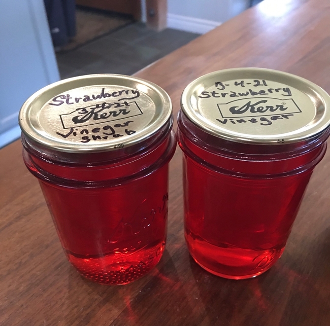 Two jars of red liquid labeled strawberry vinegar.