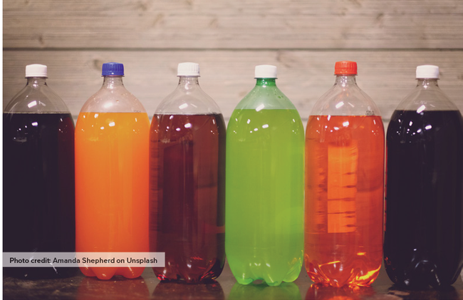 Two-liter plastic bottles of assorted colors of soda in a line.