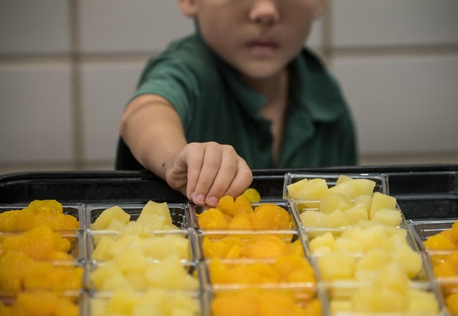A young boy reaches for fruit in the cafeteria lunch line.