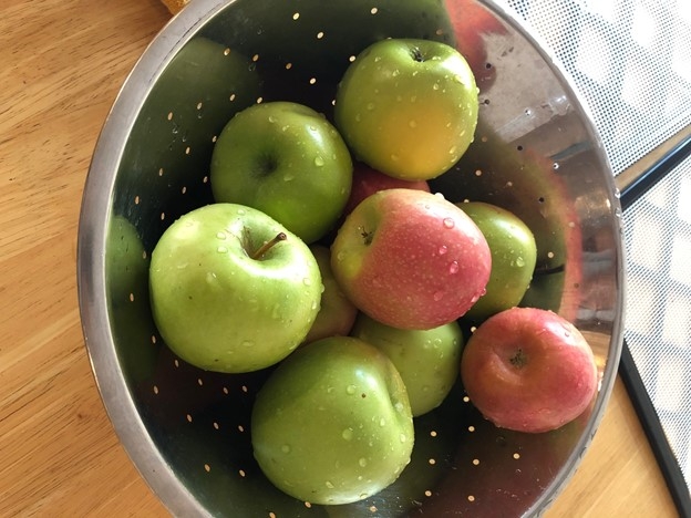 Red and green apples in a collander in the sink.