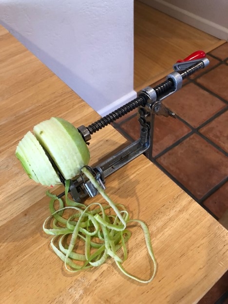 Apple half peeled in an apple peeler-corer mounted on a table.