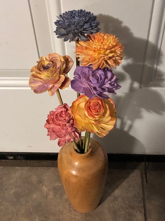 Wooden vase with 6 painted sola flowers. From tallest to shortest flower-dark blue mum, yellow and orange mum, light purple and yellow rose, lavender rose, yellow with red edged rose, and pink rose