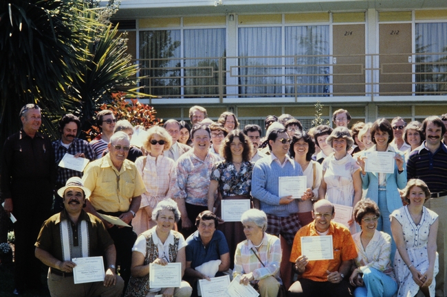 A group of freshly graduated UC Master Gardener volunteers in three rows holding up their certificates of completion.