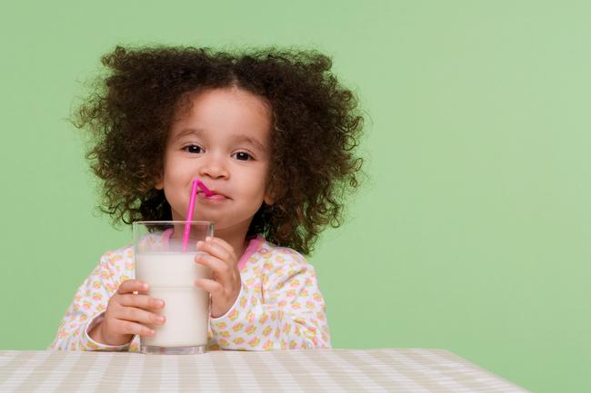 A young girl drinking milk from a cup with a straw.