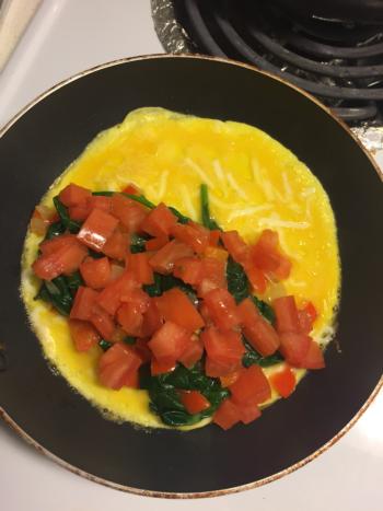 Add toppings to one side of the eggs and top with tomatoes.