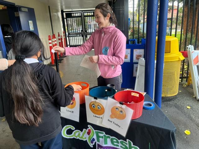 Community Nutrition Educator encouraging students to vote and provide feedback at cafeteria promotion local produce tasting