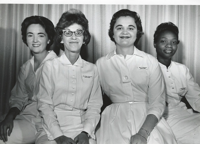 Three White women and one Black woman sit wearing uniforms uniforms.