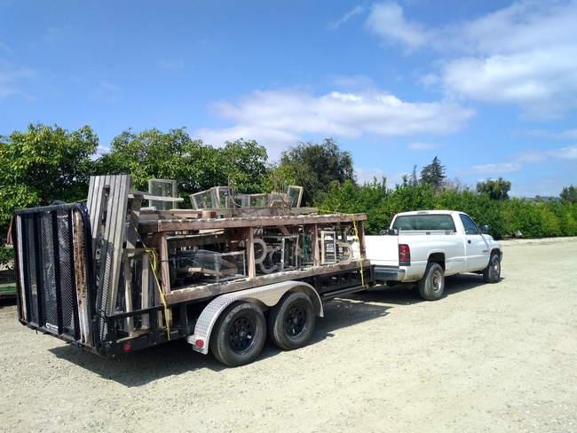 A white pickup pulling an open bed trailer filled with stuff.
