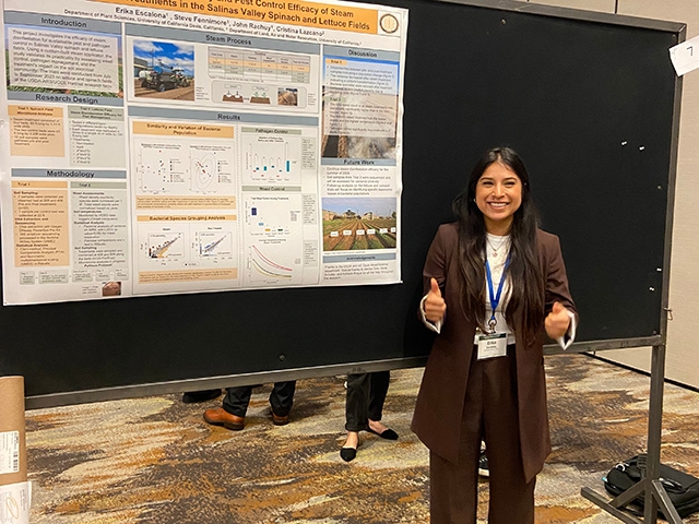 Erika gives a thumbs up as she stands beside her research poster.