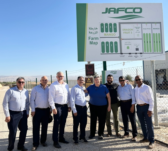 Eight people stand under a sign that reads: JAFCO farm map: mango, dragon fruit 3, engineers house, packing house, grape (prime) and mango.