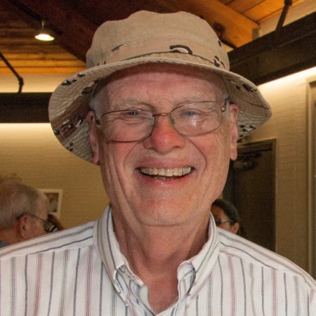 Headshot of Bill Leibhardt smiling, wearing striped, button-down shirt and a brimmed hat