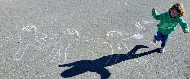 A girl plays among chalk figures drawn on pavement.
