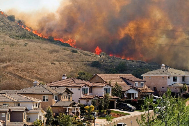 Flames and smoke line a hillside behind a street of houses.