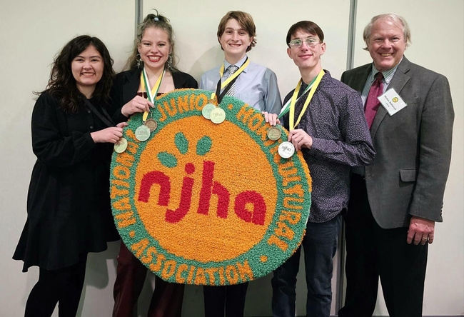 4 youth holding their medals and a round rug with the logo of NJHA, standing next to an adult in a suit and name badge