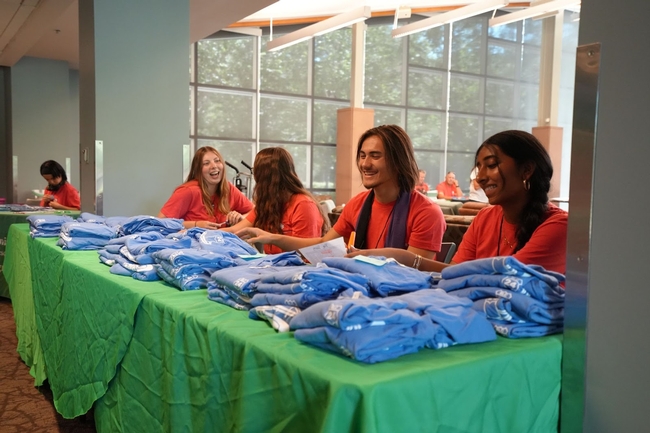 4 youth in red shirts sitting behind a table piled with folded blue shirts