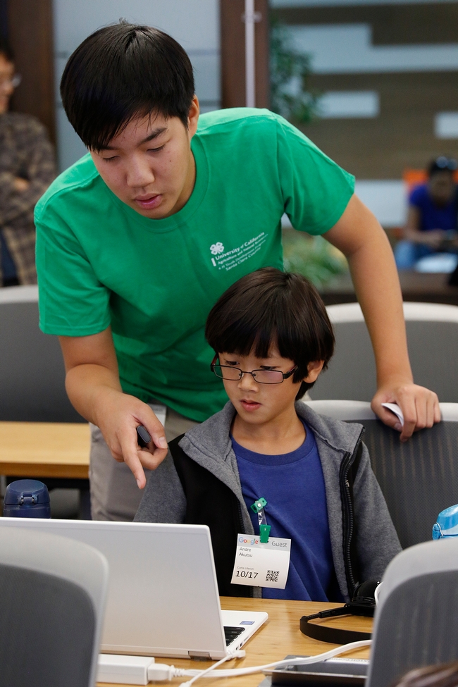 A teen teacher helping a participant with his Scratch project for Pitch Your Passion.