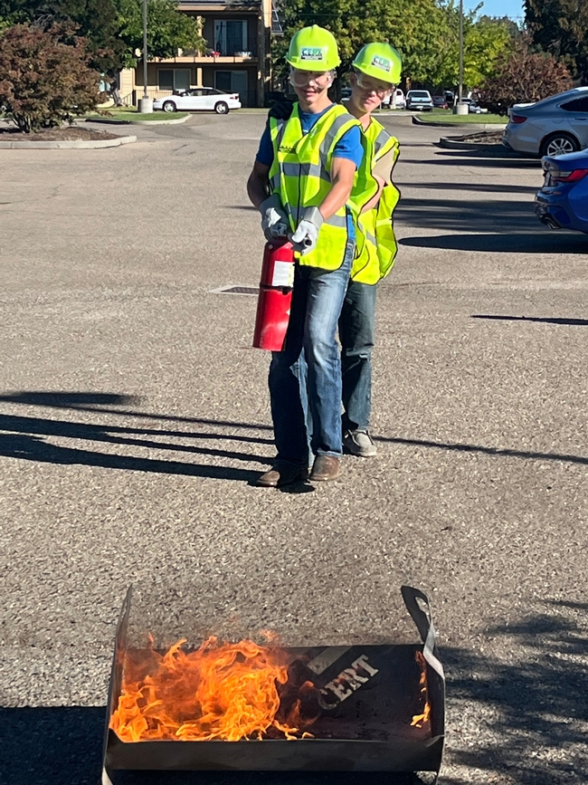 Two teens practice using a fire extinguisher in a parking lot exercise