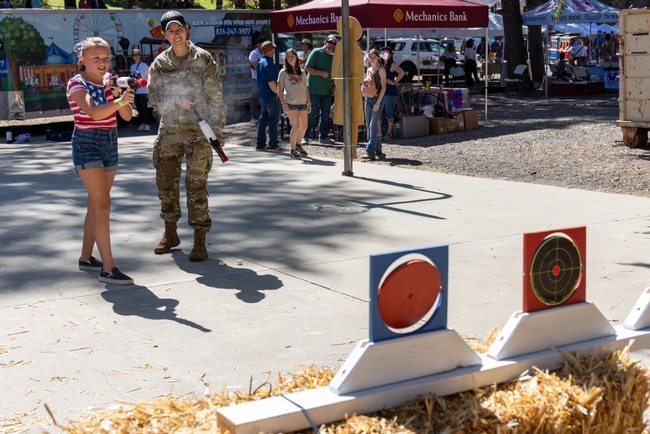 Sagen Maddalena gives instruction to a girl shooting a red, white and black plastic toy gun at a target.