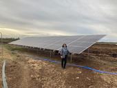 A woman stands next to an array of solar panels beside a fam field.