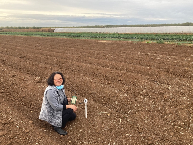 Woman holds an irrigation device while crouching in a crop field.