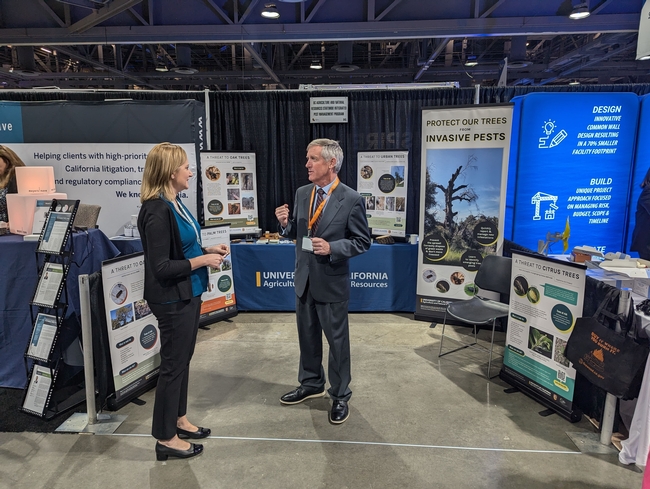 Randall Oliver talks about invasive tree pests in front of an expo table at a conference