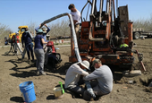 Seven people in an unplanted field collect data.