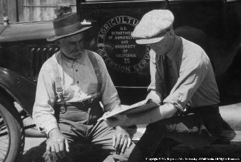 Farmer seeks assistance from UCCE farm advisor on the running board of a historic UC Cooperative Extension vehicle.