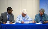 Three men sit at a table signing documents