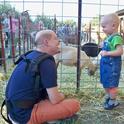 Father and son enjoy a petting zoo on a farm offering agritourism experiences.