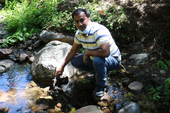 Safeez Khan crouches on stones as he samples water in a mountain stream.
