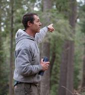 Rob York, holding a water bottle in his right hand, points into the forest with his left hand.