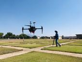 A man flies a drone over green, square test plots of hybrid bermudagrass.