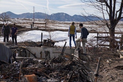Four people look around at the remains of a house and yard destroyed by the Marshall Fire.