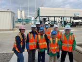 A group of young students posing in front of a water recycling facility with their tour guide.