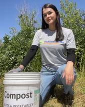 Woman crouching in a field next to a compost bucket