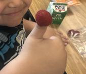 Child smiles and gives a thumbs up. There is a raspberry fixed onto the child's thumb.