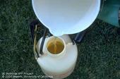 A white bucket of clear liquid being poured into a smaller container.