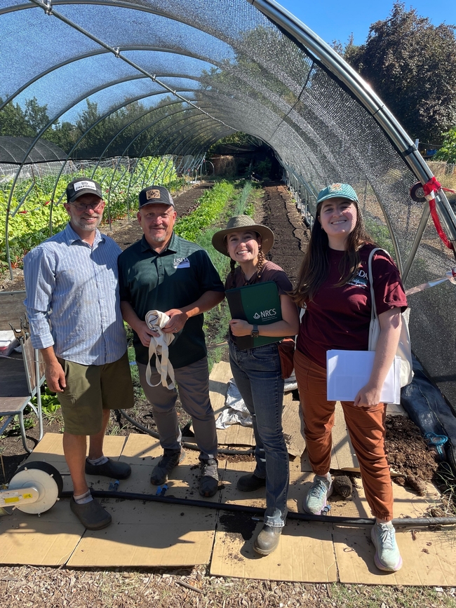 Four people stand in front of a hoop house