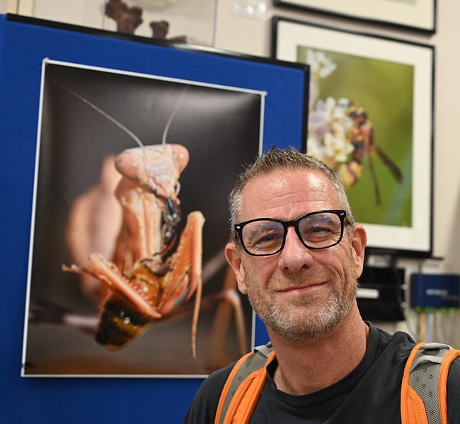 Talented photographer Ian Alexander Levin of Sacramento displayed enlarged images of praying mantises at the Bohart Museum of Entomology. Behind him is one of his images of a mantis eating a bee. Levin owns a child daycare in Sacramento and likes to share his images and critters with the youngsters in a 