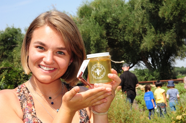 Zoe Anderson, a UC Davis undergraduate student majoring in animal biology, holds up a jar of honey bottled by Sarah the Bee Girl. Her bees foraged on vetch to produce this honey, which was the favorite of all the honeys tasted. Anderson staffed the honey-tasting table with WAS member Kari Hallopeter of Spokane, Wash. (Photo by Kathy Keatley Garvey)