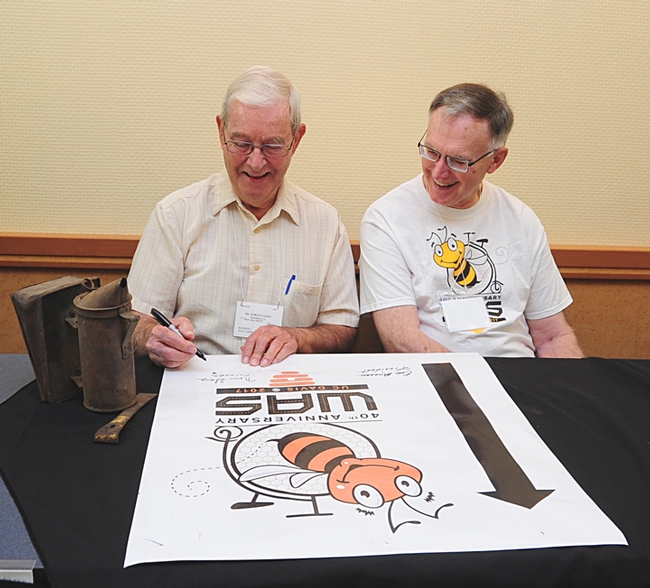 Norm Gary (left) and Eric Mussen sign a Western Apicultural Society poster. Gary initiated and spearheaded the founding of WAS and served as its first president. Mussen just finished his sixth term as president. (Photo by Kathy Keatley Garvey)